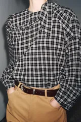 Camisa de manga larga con estampado a cuadros en blanco y negro. Presenta un cuello redondo y un pañuelo multiposición que cae en un drapeado asimétrico sobre el frente.