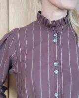 Camisa de algodón a rayas verticales blancas y azules, con cuello alto tipo gorguera con volados, cierre frontal de botones y mangas largas con puños con volados.