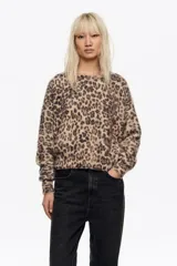 Jersey corto de textura suave y peluda con estampado animal print. Presenta escote redondo, manga larga con volumen y corte holgado.