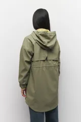 Piloto verde militar de manga larga con capucha y forro de color amarillo. Cuenta con dos bolsillos laterales con solapa, cordones ajustables, elástico en los puños, cierre y botones metálicos.