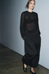 Blusa negra de manga larga abullonada, con tejido plisado y cuello redondo con abertura y botón en la espalda.