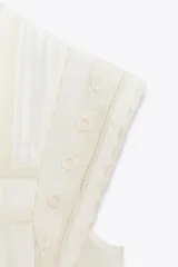 Blusa blanca sin mangas confeccionada en hilatura con viscosa y algodón. Tiene cuello redondo, detalle de bordados a contraste y cierre en espalda con abertura y botón.