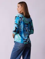 Remera de algodón estampada con flores en tonos celeste, azul y verde, sobre fondo negro. Tiene mangas 3/4 y escote cuadrado.