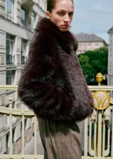 Chaqueta de pelo sintético en color marrón oscuro, con diseño recto, cuello solapa, cierre frontal con cremallera y manga larga.