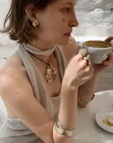 Collar artesanal con dije central de metal con textura orgánica irregular que evoca una ostra. El dije está montado sobre un cordón de algodón natural, permitiendo un uso versátil y regulable.