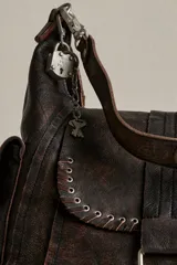 Cartera hobo de cuero marrón con efecto desgastado, solapa frontal con ojales metálicos y tira con hebilla. Cuenta con bolsillos laterales con solapa y herrajes metálicos plateados.