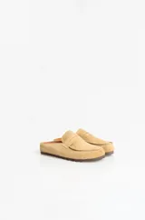 Zuecos tipo mule de estilo mocasín, confeccionados en material símil gamuza color beige. Presentan punta redondeada, tira frontal estilo penny y costuras decorativas al tono, con una base plana de 1 cm.