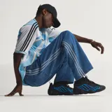Pantalón de denim azul de corte holgado, tiro medio y diseño clásico con las tres tiras características de Adidas a lo largo de los laterales.