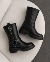 Botas de caña media de cuero negro, con suela track gruesa y taco cuadrado. Presentan tiras con anillas metálicas y tachas decorativas alrededor del tobillo y la caña.