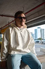 Hoodie canguro blanco de diseño oversize, con capucha, bolsillo frontal tipo koozban y sutil bordado monocromático en el pecho.