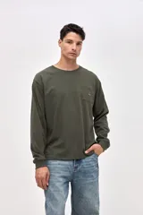 Remera de manga larga color verde oliva, confeccionada en algodón pesado con textura suave. Presenta un bolsillo frontal en el pecho con un pequeño bordado de la marca y puños acanalados en las mangas.