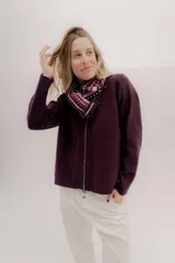 Polera tejida en lambswool color beige, con cuello alto y diseño de intarsia en tonos marrones y grises. Presenta botones forrados en el cuello para modular la apertura.