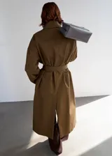 Abrigo largo oversize de algodón color verde militar, con cuello camisero, cierre delantero de botones ocultos, bolsillos laterales y tiras decorativas en el frente.