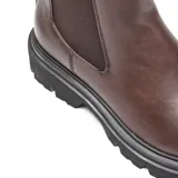 Bota tipo Chelsea de caña media en color marrón, confeccionada en material sintético con acabado liso. Presenta paneles laterales elásticos, tirador trasero y una suela chunky de goma negra con plataforma dentada.