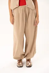 Pantalon tipo babucha de color beige, con silueta relajada y acabado suave tipo piel de durazno. Presenta cintura regulable con cordón y elástico en los tobillos que genera una forma abuchonada.