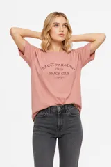 Remera de manga corta color rosado, con diseño holgado, cuello redondo a la base y estampa frontal en tono bordó con la inscripción "Saint Paradiso Italia Beach Club 1991".