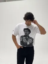 Remera blanca de algodón con estampa fotográfica frontal de Ayrton Senna con su traje de piloto de Fórmula 1. Presenta un corte holgado y cuello redondo.
