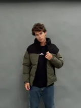 Campera puffer con capucha, diseño bicolor en verde oliva y negro, cierre frontal y bolsillos laterales.