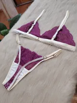 Conjunto de lencería compuesto por un bralette triangular y una tanga, confeccionados en encaje color fucsia con terminaciones y breteles en color crema. El bralette presenta un diseño sin aros con bordes festoneados, mientras que la tanga cuenta con tiras laterales regulables.