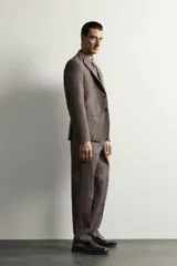 Pantalón de traje regular fit marrón con sutil estampado a cuadros, confeccionado en mezcla de lino y lana. Cuenta con bolsillos delanteros, bolsillos traseros de doble vivo con botón y raya marcada en el centro de las piernas.