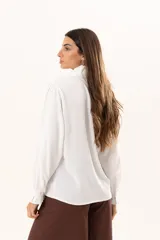 Camisa blanca de cuello alto con volados frontales a lo largo de la botonadura, manga larga con puños con volados y cierre frontal con botones.