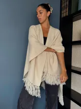 Ruana tejida a mano en punto arroz con lana merino, presenta un diseño envolvente con flecos en los extremos.