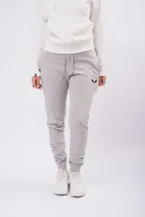 Pantalón de jogging color gris melange, con cintura elástica ajustable mediante cordón y puños acanalados en los tobillos. Presenta un pequeño logo bordado en color negro en la parte superior del muslo izquierdo.