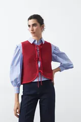Chaleco de punto color rojo con efecto jaspeado, diseño sin mangas y cierre frontal mediante tres lazos ajustables.