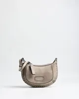 Bandolera de diseño semicircular en color taupe, confeccionada en símil cuero. Presenta detalles de tachas metálicas plateadas en los bordes, placa con logo de la marca en el frente y correa ajustable para hombro o cruzada.