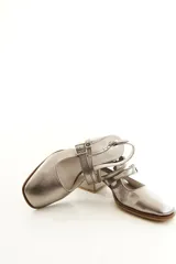 Zapatos tipo Mary Jane de charol color negro, con taco bloque, talón descubierto y doble tira frontal con hebillas metálicas.