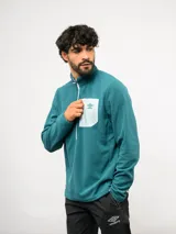 Buzo de entrenamiento Umbro con medio cierre frontal, cuello alto y bolsillo en el pecho de nylon con cierre. Presenta una textura sutil en el tejido y logo de la marca estampado en el bolsillo.