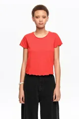 Remera corta de corte ajustado confeccionada en 100% algodón orgánico, de color rojo, con escote redondo, mangas cortas raglán y terminaciones con ondas en puños y dobladillo.