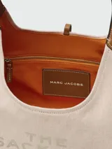 Cartera tipo hobo de Marc Jacobs, confeccionada en lona color beige con detalles en cuero negro. Presenta el logo estampado en el frente y una correa de hombro ajustable.