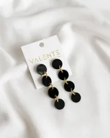 Par de aros colgantes con círculos negros unidos por argollas doradas.