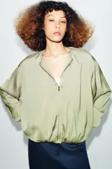 Cazadora bomber fluida de color verde, con cuello redondo, manga larga abullonada, bolsillos frontales y cierre de cremallera metálica.
