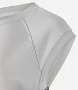 Remera deportiva de mujer color blanco hueso, con cuello redondo y mangas cortas tipo raglán con pespuntes visibles. Presenta un ruedo inferior más ancho y ajustado.