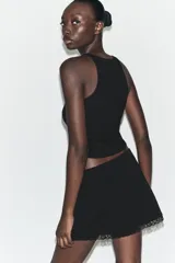 Minifalda negra de tiro medio y cintura elástica, con detalle de encaje a tono en el borde inferior.
