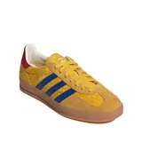 Championes Adidas Gazelle Indoor con exterior de gamuza amarilla y estampado geométrico sutil. Presenta las tres tiras laterales en azul, detalle en el talón en color rojo y suela de caucho color caramelo.
