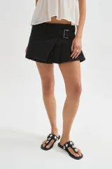 Minifalda de jean negra con diseño cruzado, cierre de hebilla metálica y detalle de tablones plisados en el lateral.