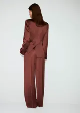 Pantalón largo de tiro medio en tejido satinado color marrón, con diseño de pernera recta, trabillas para cinturón, pinzas delanteras, bolsillos laterales y bolsillos de ribete en la parte posterior. Cierre frontal oculto con botón, gancho y cremallera.