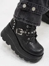 Botas de plataforma estilo borceguí, color negro, confeccionadas en materiales sintéticos. Presentan una suela de goma dentada, cordones frontales y una tira decorativa con hebilla metálica y tachas plateadas en la parte superior.
