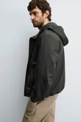 Parka de tejido técnico con acabado engomado, cuello subido y capucha ajustable. Presenta cierre frontal con cremallera oculta bajo solapa con botones a presión, bolsillos laterales de vivo y mangas largas con puños ajustables.