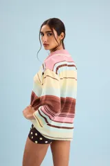 Buzo de algodón tejido, de calce relajado y silueta amplia con diseño de rayas horizontales en tonos pastel de amarillo, celeste, rosa y marrón. Tiene cuello tipo polo con terminación artesanal en crochet y mangas amplias.