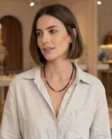 Collar de diseño minimalista compuesto por pequeñas cuentas negras intercaladas con cuentas cilíndricas de piedra natural en tono coral y detalles en dorado.