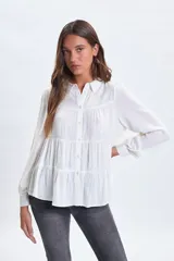 Camisa blanca de corte holgado con diseño de paneles escalonados, cuello clásico, cierre frontal con botones y mangas largas con puños.