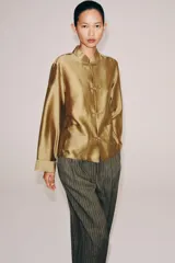 Camisa de estilo oriental confeccionada en mezcla de lyocell con acabado satinado. Presenta cuello redondo, manga larga con puños rectos, bolsillos de plastrón y cierre frontal mediante alamares.