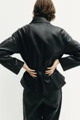 Chaqueta de efecto piel con cuello solapa, manga larga y cierre frontal con cremallera. Presenta cintura elástica que entalla la silueta y bolsillos decorativos en el frente.