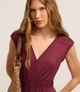 Mono largo de viscosa color borgoña, con corte flare, escote en V, sin mangas, elástico en la cintura y lazo en el cuello.