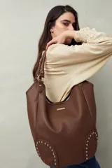 Bolso shopper marrón de símil cuero texturizado con asas cortas y detalles de tachas metálicas.