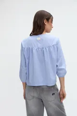 Camisa de manga larga con diseño a rayas celestes y blancas, cuello redondo y cartera de botones frontales. Presenta mangas con puños elásticos.
